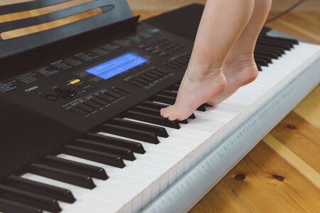 A little girl in a burgundy suit plays a synthesizerの写真素材