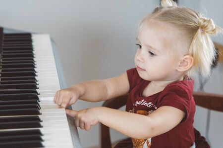 A little girl in a burgundy suit plays a synthesizerの写真素材