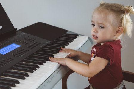 A little girl in a burgundy suit plays a synthesizerの写真素材