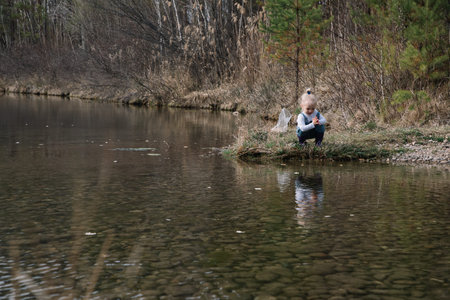 Little girl in rubber boots catches and feeds fish on the river in a jar.の写真素材