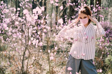 Girl in a medical mask among flowersの写真素材