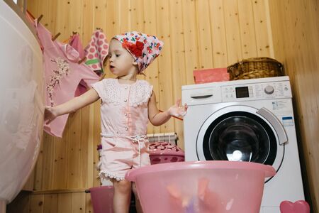 Little girl sitting bathes a doll in a basin on the floor in the bathroomの写真素材