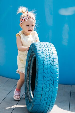 Little girl in a bright outfit with colored tires on a blue backgroundの写真素材