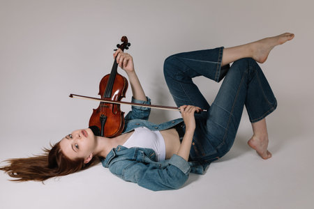 The girl in jeans and barefoot plays the violin on a white background.