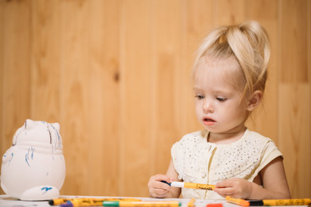 Little girl paints a piggy bank with markers