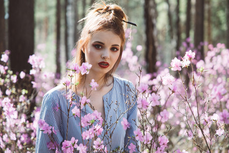 A girl dressed in Japanese style in a flowering forest among pink flowers.の写真素材