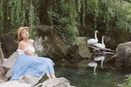 A girl in a blue skirt, white top and hat with a retro camera and a bunch of lavender walks in a beautiful forestの写真素材