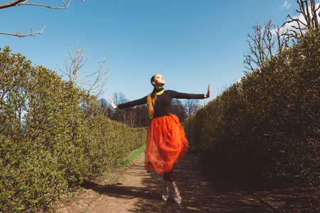 Model girl, ballerina in a red tutu, black turtleneck, high heel shoes in a city gardenの写真素材