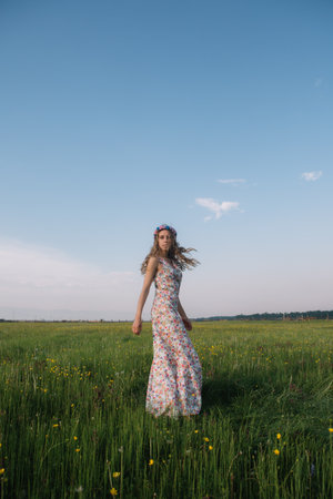 Girl in a floral dress and a wreath in the field with yellow flowersの写真素材