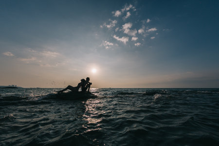 Young couple guy with a girl sitting on a rock washed by the sea on a sunset background.の写真素材