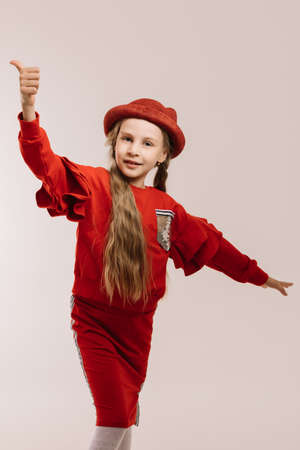 Little girl in a red suit and hat posing on a light backgroundの写真素材