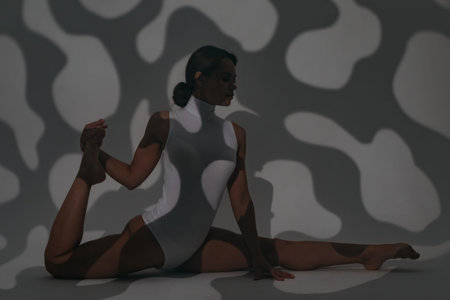 Girl dancer doing stretching in the studio while painting light with openwork shadows