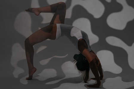 Girl dancer doing stretching in the studio while painting light with openwork shadows