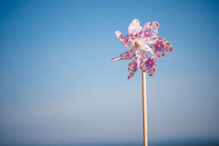 Toy windmill close-up on the background of sand of the sea and sky, children's game toy colored blades pinwheel weather vane, sea summer sun weekend vacation, shore wave foam shellsの写真素材