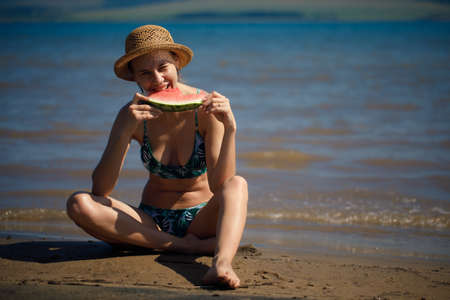 Portrait of smiling woman relaxing holding and eating a slice of watermelon on the tropical beach.Summer vacationsの写真素材