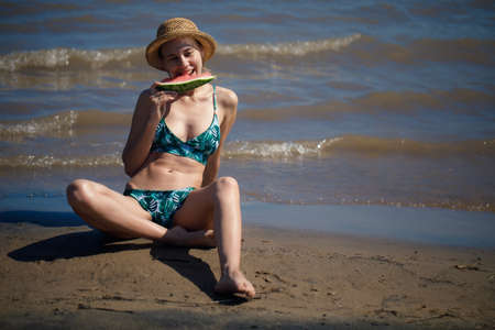 Portrait of smiling woman relaxing holding and eating a slice of watermelon on the tropical beach.Summer vacationsの写真素材