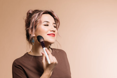 Girl makeup artist in glasses on a beige background shows cosmetics