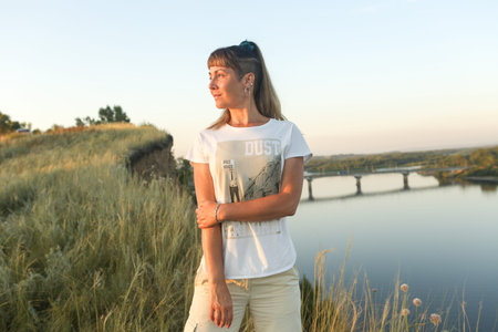 A young woman on a steep cliff by the river on a warm summer evening.