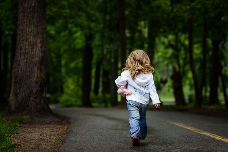 Little blonde girl walks away to dark park aloneの写真素材