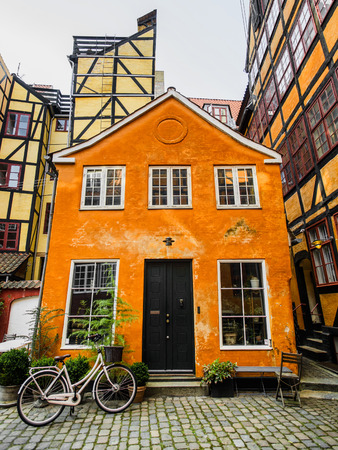 Cute hipster rose bike with basket at doors of colorful orange old town danish houseのeditorial素材