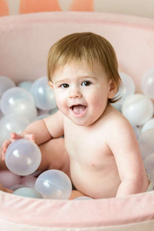 cute baby girl playing with balls in ball pool at home, pastel pink colors, close upの写真素材