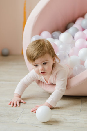 cute baby girl playing with balls in ball pool at home, pastel pink colorsの写真素材