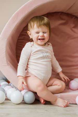 cute baby girl playing with balls in ball pool at home, pastel pink colorsの写真素材