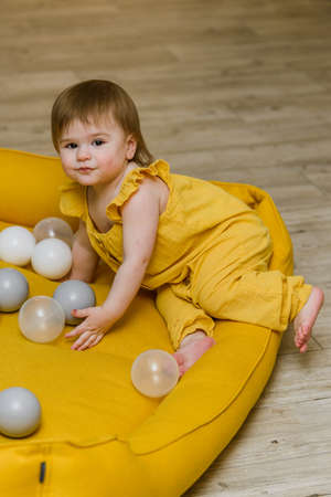 1 year birthday baby girl playing with ball pool balls with festive balloons on background, yellow and gray colorsの写真素材