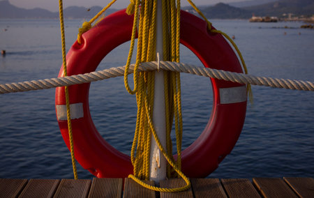 A red lifebuoy and yellow ropes are hanging on the pier. Sea in the background.