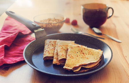 Simple breakfast: three pancakes in a black pan, buckwheat porridge in a bowl, a dark glass with a...
