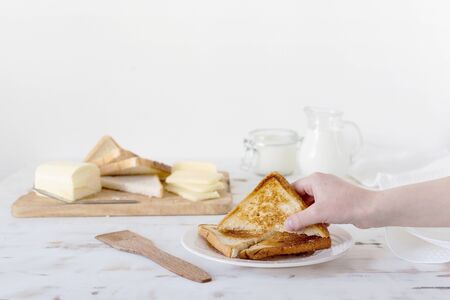 Hand takes fried croutons from the table. In the background - butter, cheese, milk, sour cream. Wooden white background. Country style. Breakfast.の写真素材