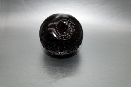 Black plum in a spray of water close-up on a light gray background