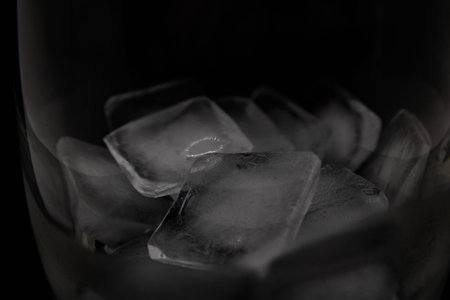 Glass with melting ice cubes close up on a black background