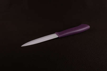 Ceramic kitchen knife with purple plastic handle on dark brown backgroundの写真素材