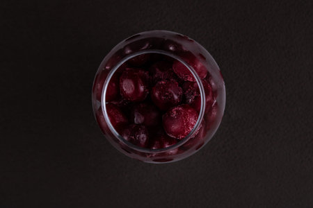 Crystal glass with frozen cherries top view on dark brown background