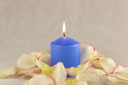 Blue candle in rose petals close-up on a light beige backgroundの写真素材