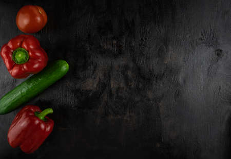 Two red peppers, a cucumber and a tomato on a dark wooden background, copy spaceの写真素材