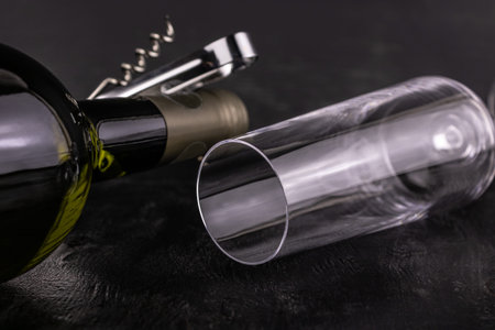 Wine bottle, glass and corkscrew close-up on dark wooden background