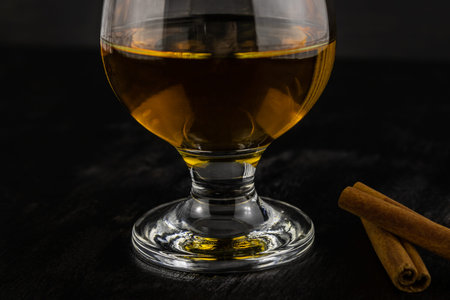 A glass of cognac and cinnamon sticks in close-up on a dark wooden background