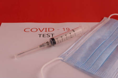 Syringe and mask in blue on a white sheet with the inscription "covid-19"の写真素材