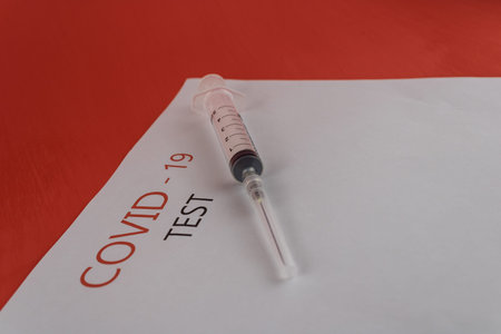 White sheet of paper with text: covid 19 test and a syringe close-up on a red background