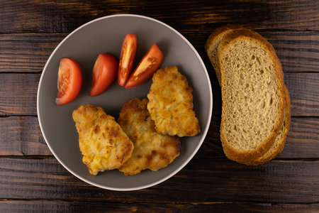Pork fried in batter, tomato slices and bread on a dark wooden background, top view.の写真素材