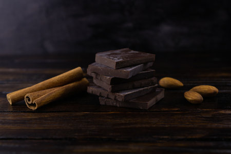 Chocolate slices, cinnamon and almonds close up on a dark wooden background.の写真素材