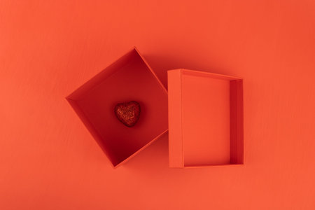 Red gift box with a heart inside on a red background, top view.