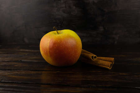 Juicy, ripe apple and cinnamon sticks close-up on a dark wooden background.の写真素材