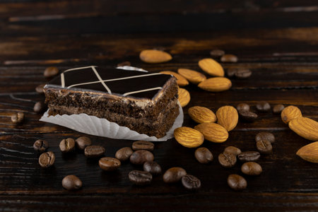 chocolate-coated sponge cake with a scattering of coffee beans and almonds on a wooden background close-upの写真素材