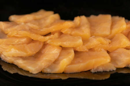 Delicious slices of lightly salted salmon close-up on a black plate.の写真素材