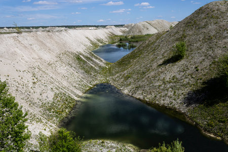an old chalk quarry overgrown with green young plants with clear water at the foot landscapeの写真素材