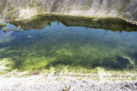 clear blue water in an abandoned chalk quarry with steep banks overgrown with grass and bushes landscapeの写真素材