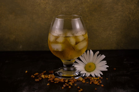 A glass of cognac with ice with a scattering of amber and a daisy flower on a dark background...